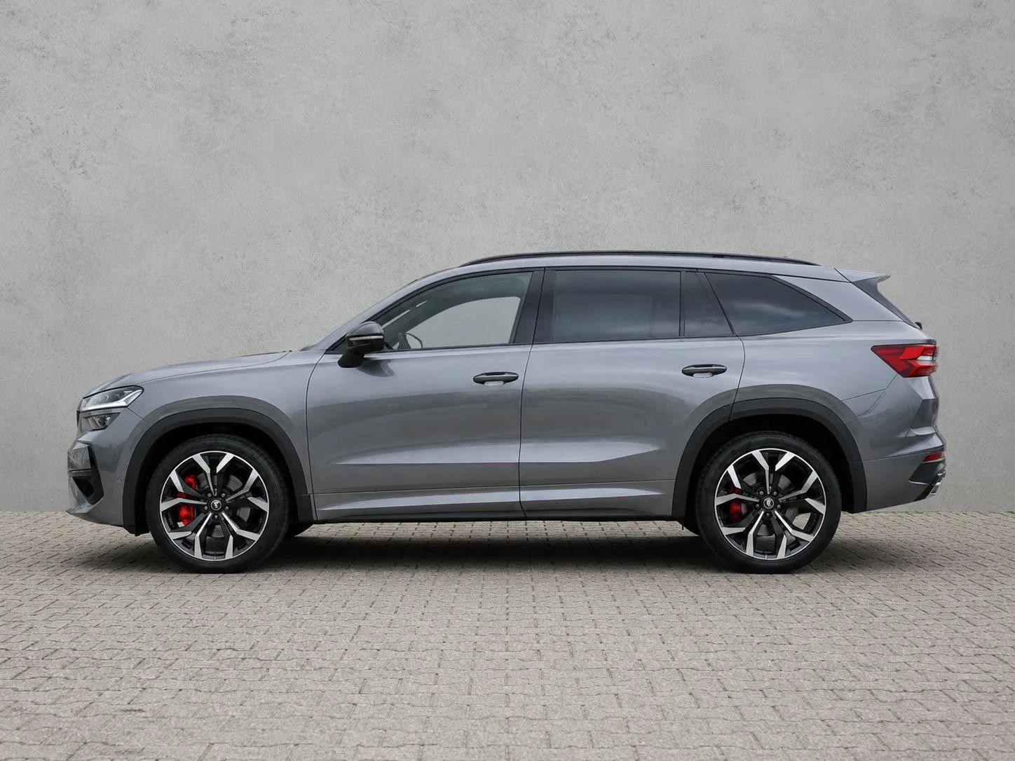 Szara Škoda Kodiaq RS 2026, profil boczny, duże felgi i czerwone zaciski hamulców, na tle jasnej ściany
