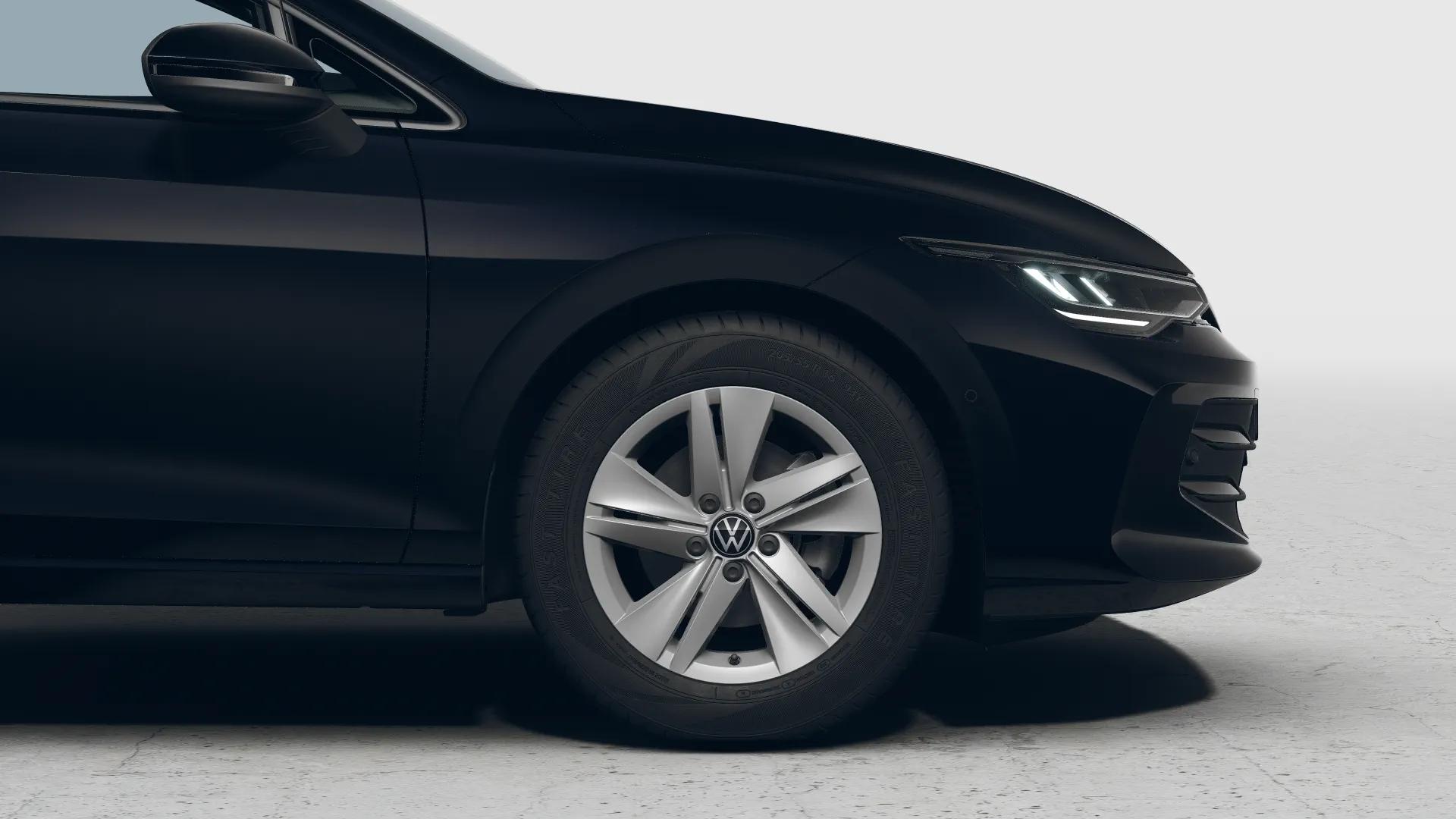 Zbliżenie przedniego koła i reflektora ciemnego Volkswagena Golfa Varianta na jasnym tle